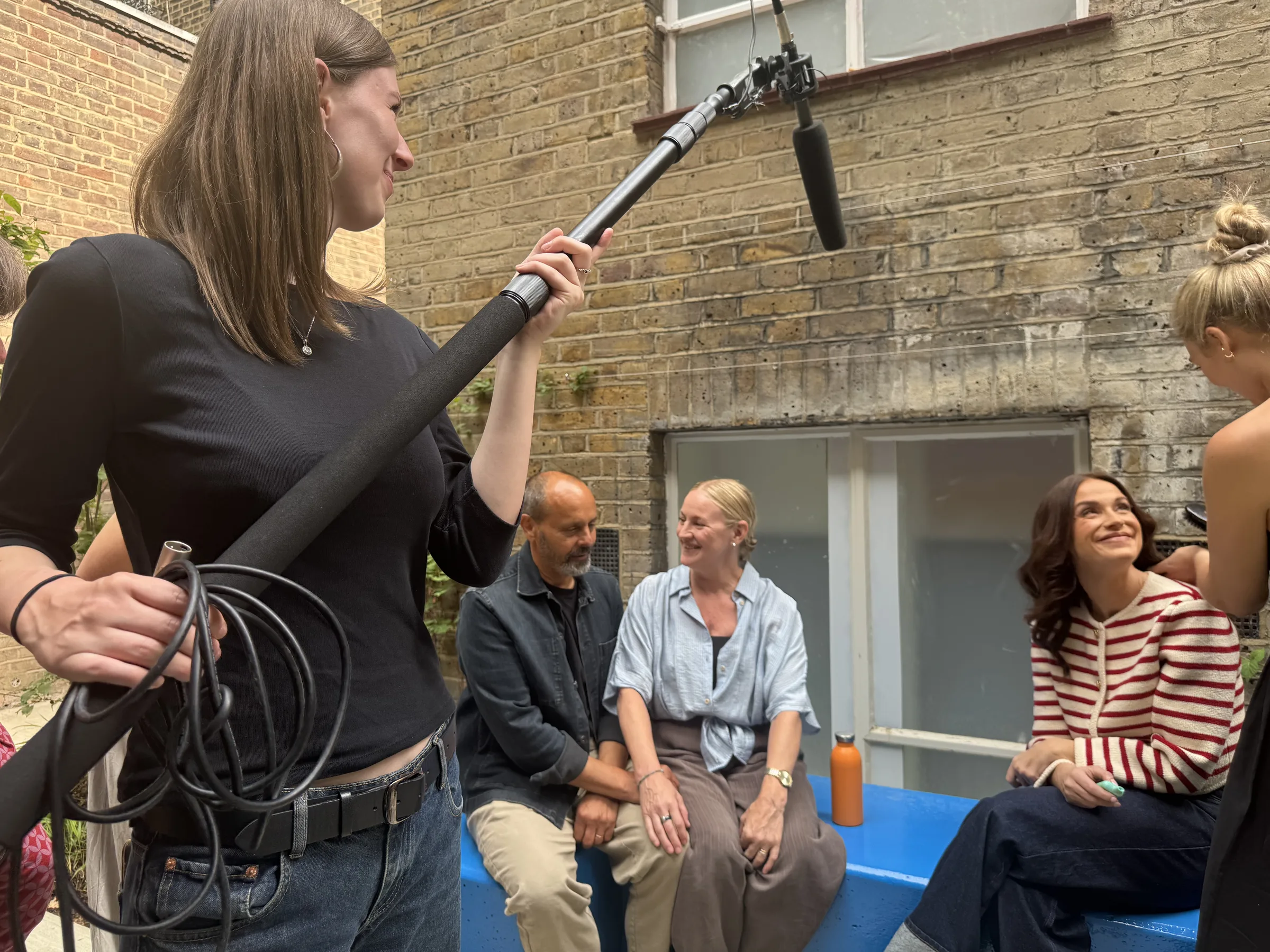 A boom operator holding a microphone over contributors during a location shoot