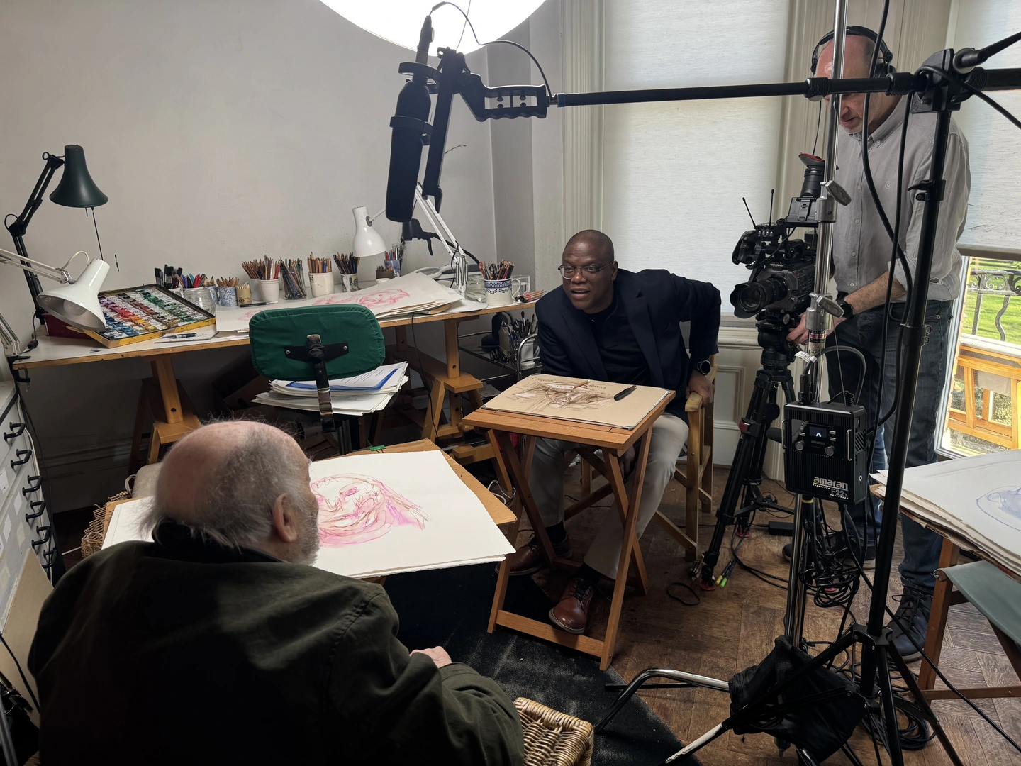 Behind the scenes of a documentary interview — a camera crew films a contributor in an artist's studio