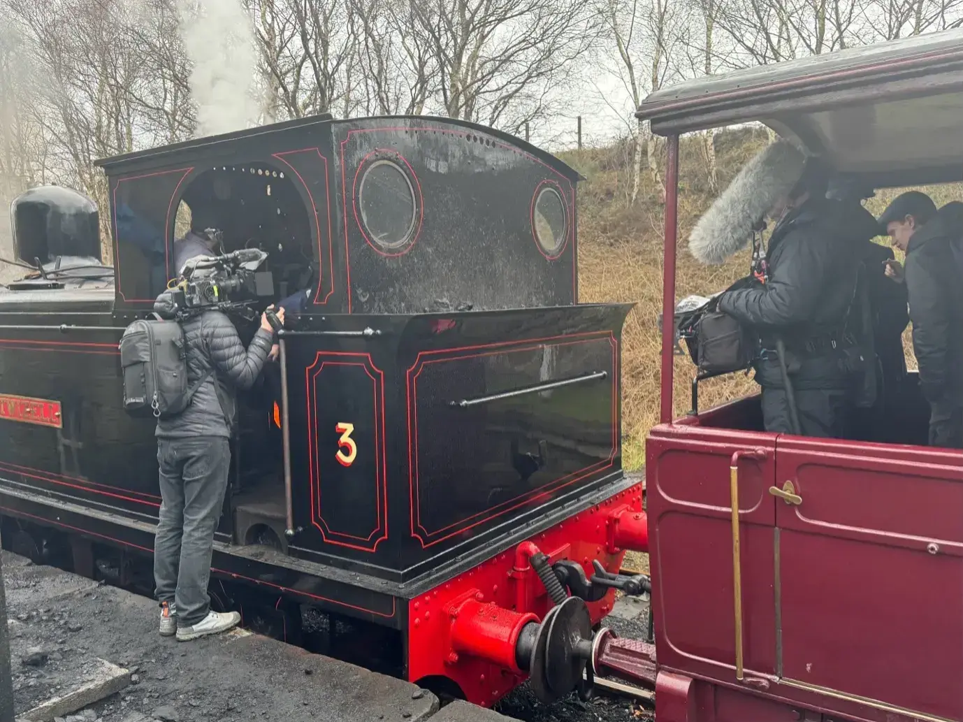 A camera operator films a black steam locomotive at a station, behind-the-scenes on The World's Oldest Railway for BBC Our Lives