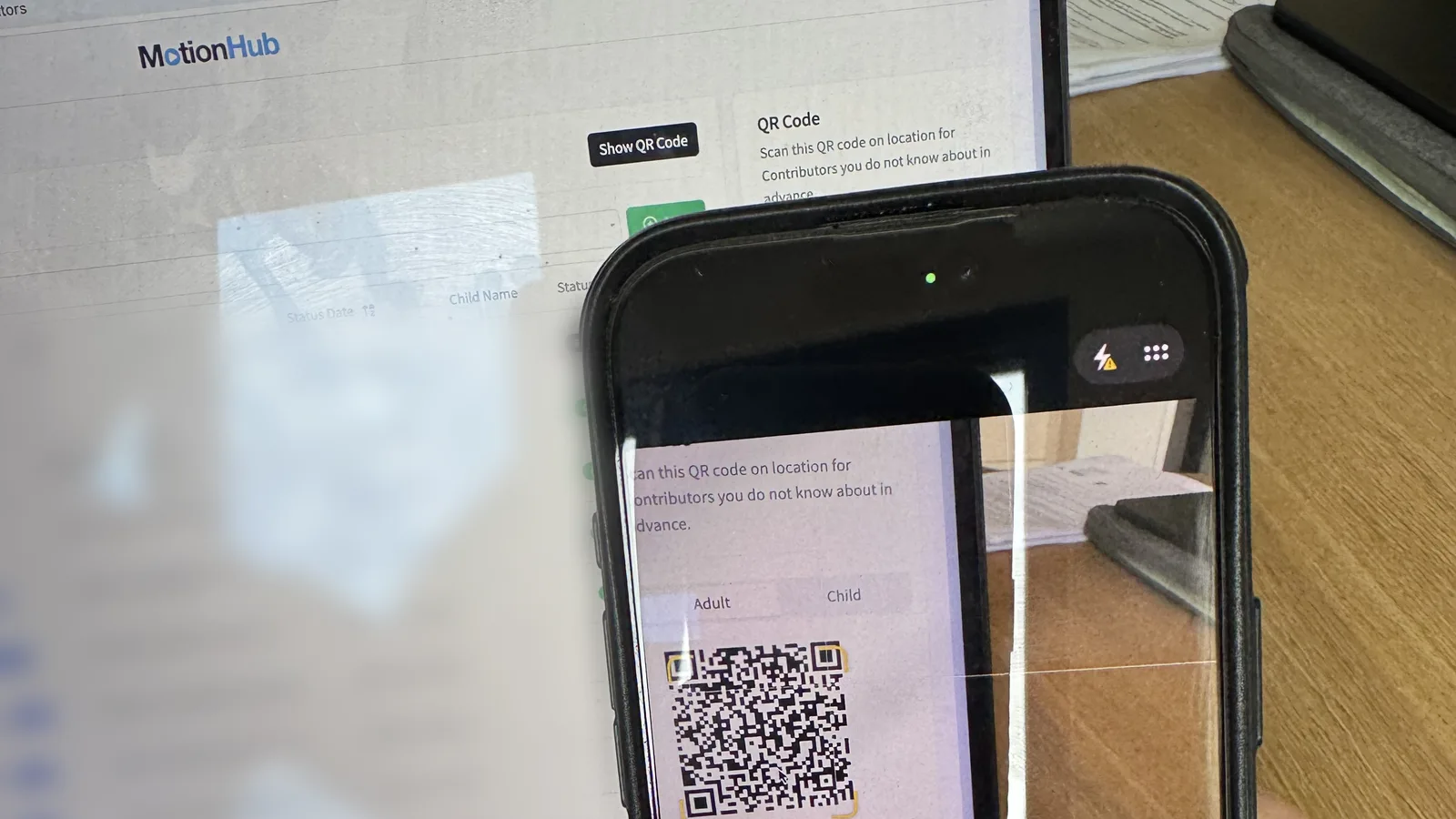 A phone scanning a contributor sign-up QR code displayed in MotionHub on a laptop screen